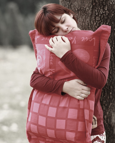 Frau mit rotem Kissen lehnt an einen Baum